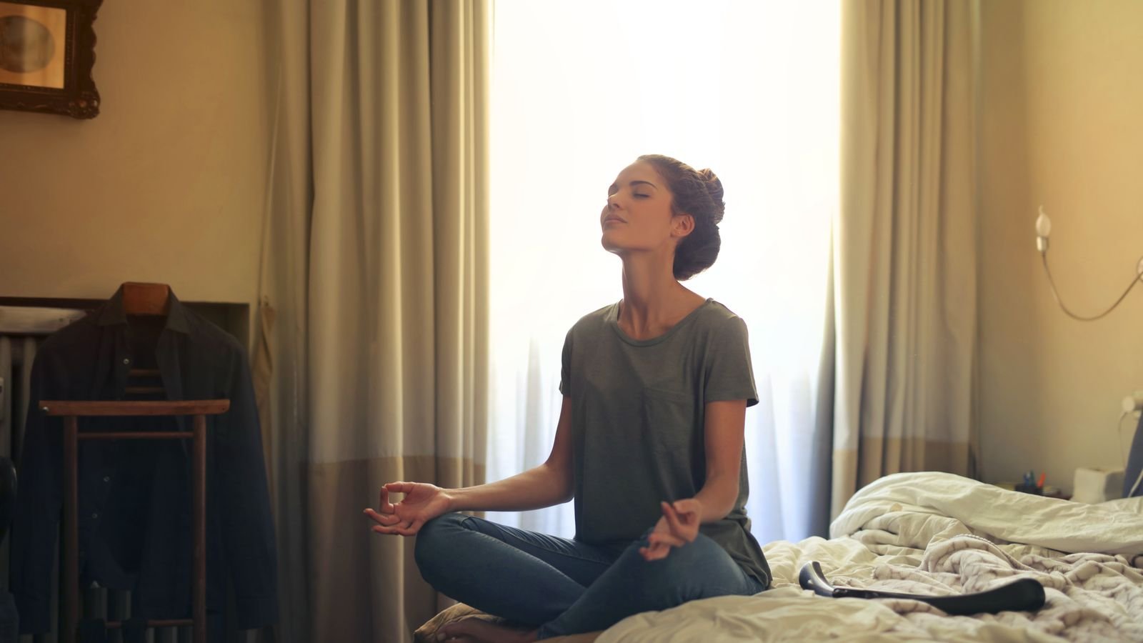 Woman meditating on a bed in soft morning light